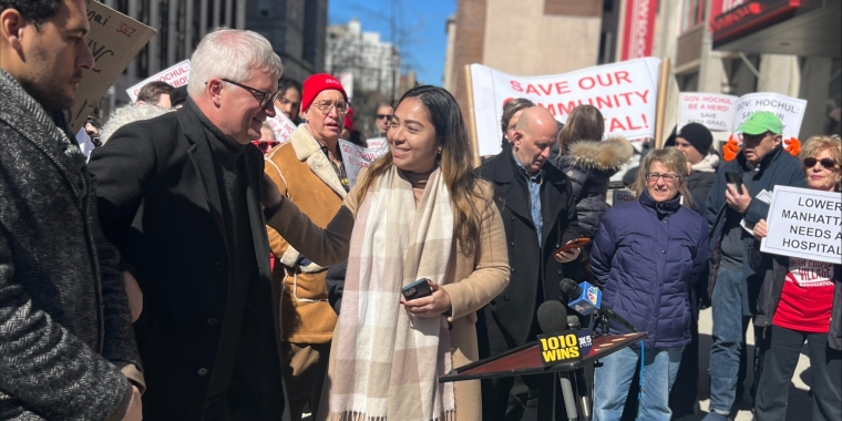 Senator Gonzalez stands with colleagues while standing outside in front of a red and white banner that says "Save Our Community Hospital"